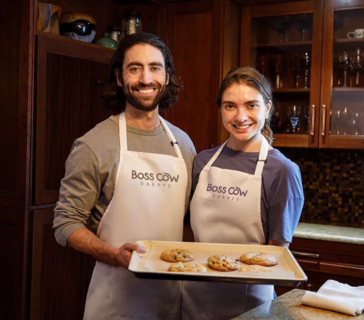 Founders Kevin and Samantha in Boss Cow Bakery aprons, presenting organic cookies.
